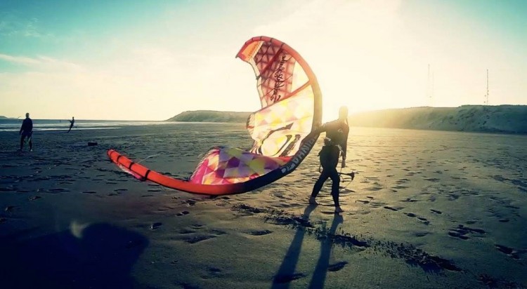 Personne marchant sur la plage avec un kite sous le bras au coucher de soleil.