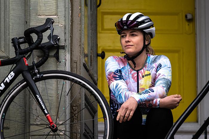 Femme avec des vêtements de vélo de route Brava assise sur un bas de porte en ville