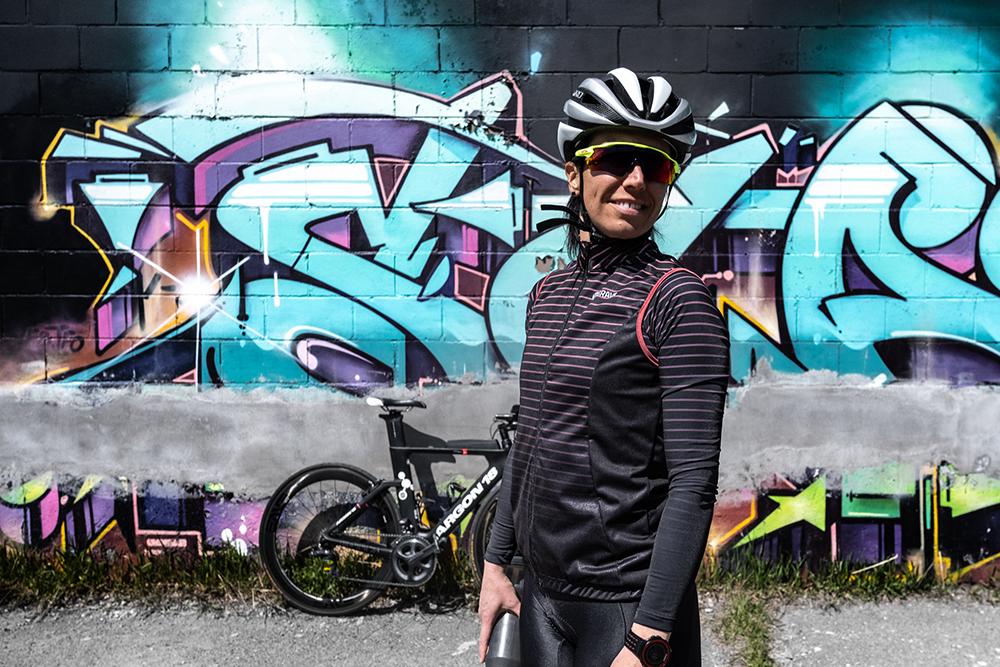 Femme avec vêtements de vélo de route Brava devant un graffiti